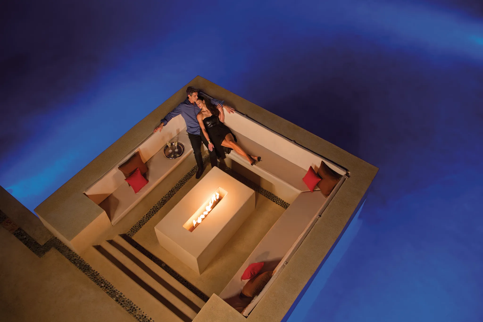 Romantic couple relaxing beside a private pool island firepit lounge at Secrets Playa Mujeres Golf & Spa Resort.