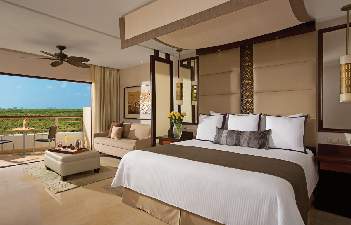 Junior Suite Garden View king bedroom with canopy bed, sitting area, and balcony at Secrets Playa Mujeres Golf & Spa Resort.